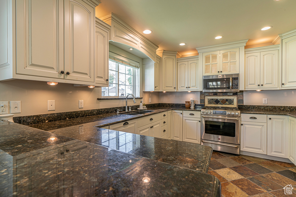 Kitchen with sink, white cabinetry, stainless steel appliances, and dark stone counters