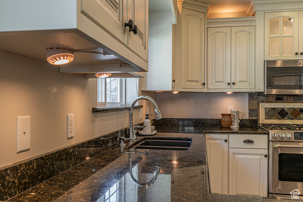 Kitchen with dark stone countertops, white cabinets, stainless steel appliances, and sink