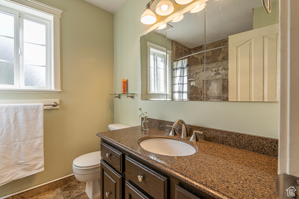 Bathroom with a healthy amount of sunlight, vanity, a tile shower, and toilet