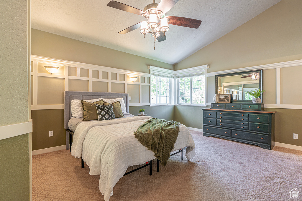 Bedroom featuring a textured ceiling, vaulted ceiling, light colored carpet, and ceiling fan