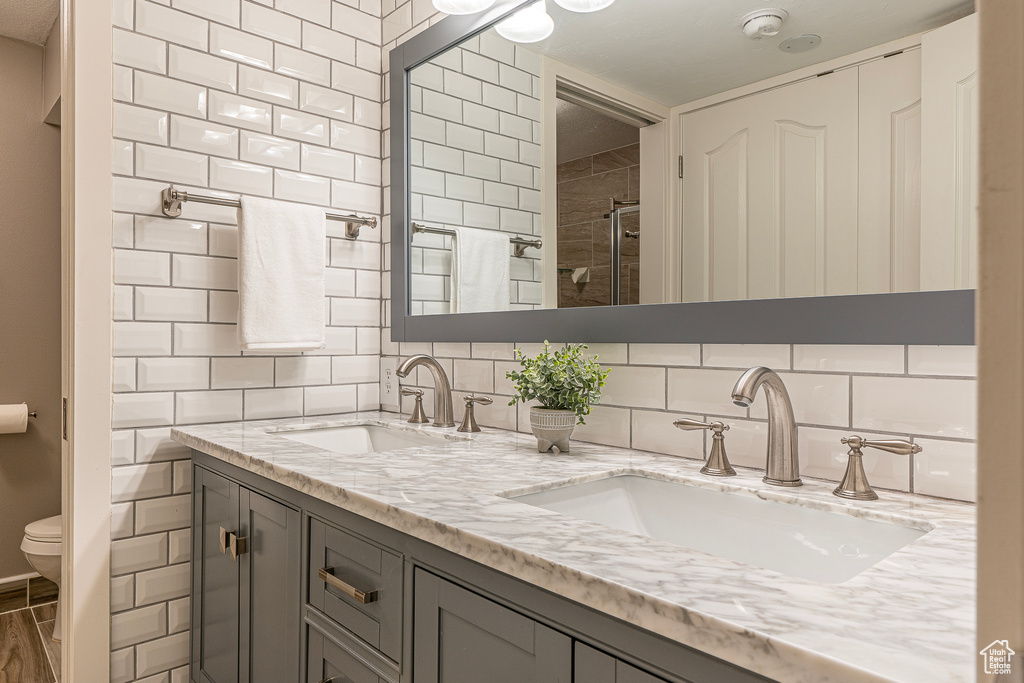 Bathroom featuring vanity, walk in shower, toilet, and tasteful backsplash