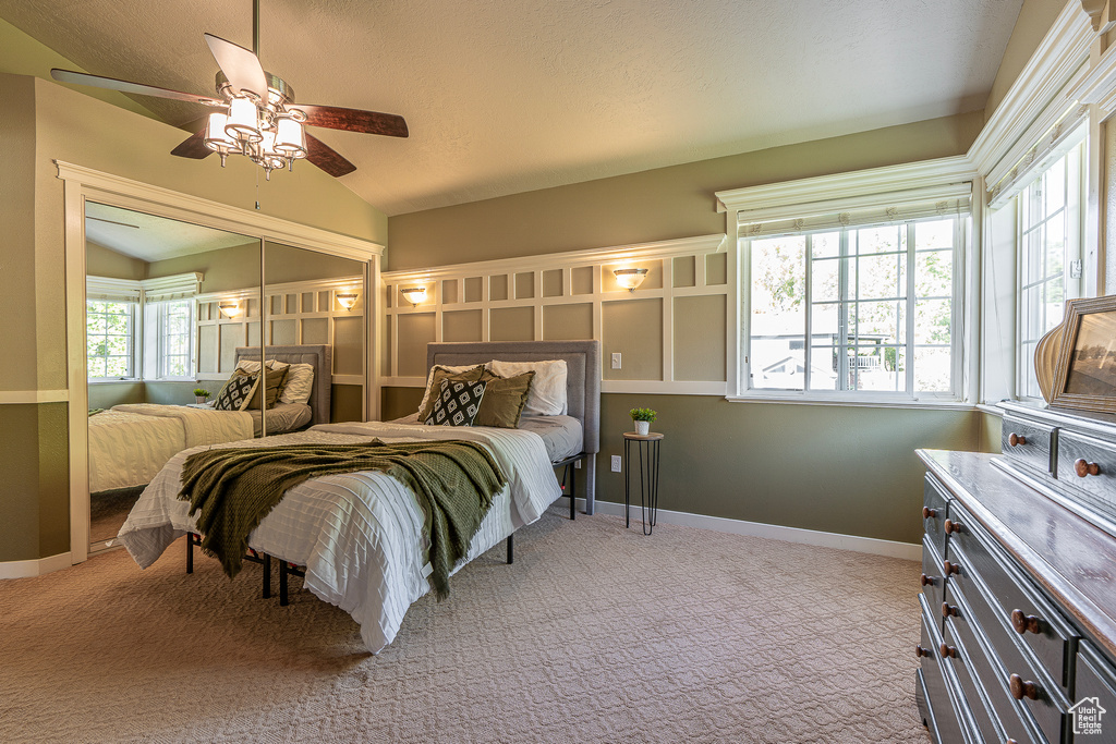 Carpeted bedroom featuring lofted ceiling, multiple windows, a closet, and ceiling fan