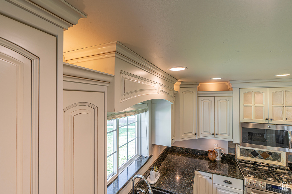 Kitchen with appliances with stainless steel finishes, ornamental molding, white cabinets, and dark stone counters