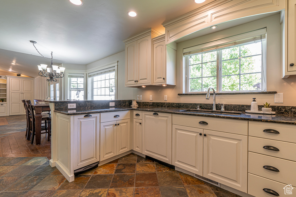 Kitchen with sink, a notable chandelier, decorative light fixtures, and dark stone countertops