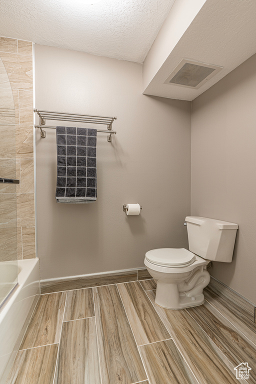 Bathroom with shower / washtub combination, a textured ceiling, and toilet