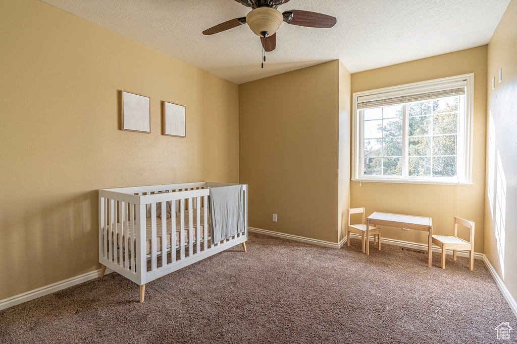 Unfurnished bedroom featuring ceiling fan, carpet, a textured ceiling, and a nursery area