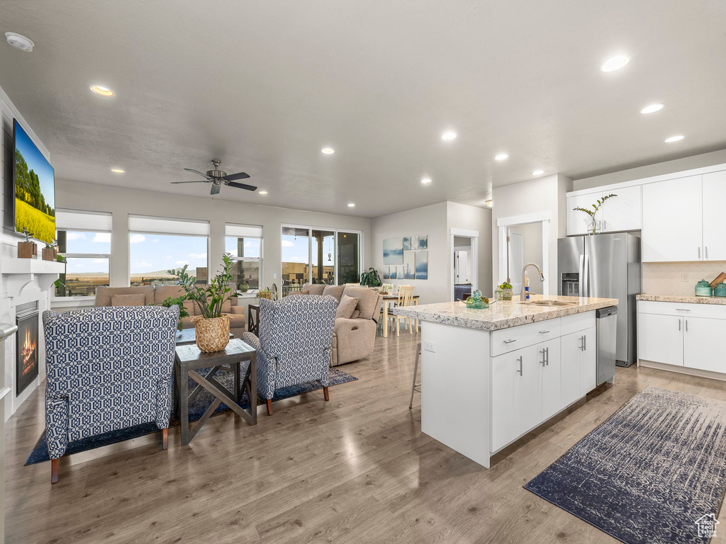 Kitchen featuring appliances with stainless steel finishes, sink, light hardwood / wood-style floors, white cabinets, and a kitchen island with sink