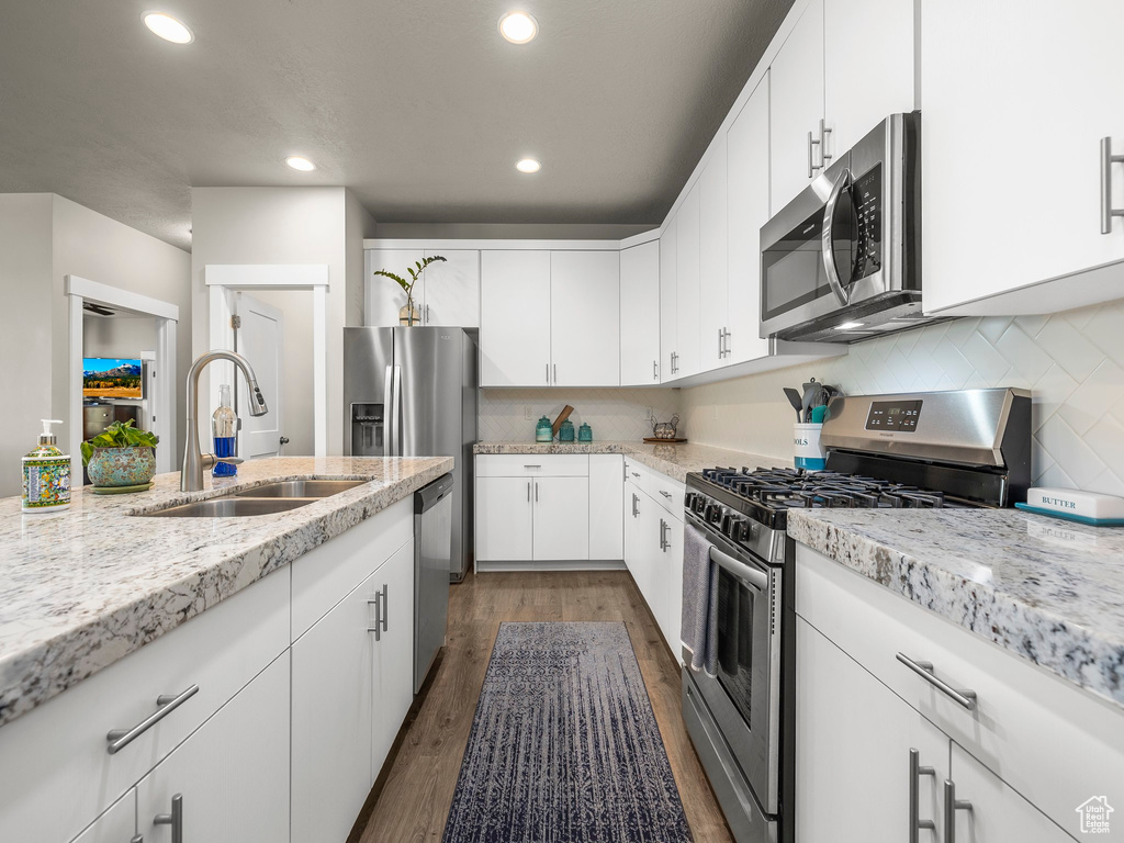 Kitchen featuring sink, light stone countertops, white cabinets, appliances with stainless steel finishes, and dark hardwood / wood-style flooring