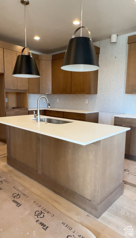 Kitchen with sink, a kitchen island with sink, hanging light fixtures, and light wood-type flooring