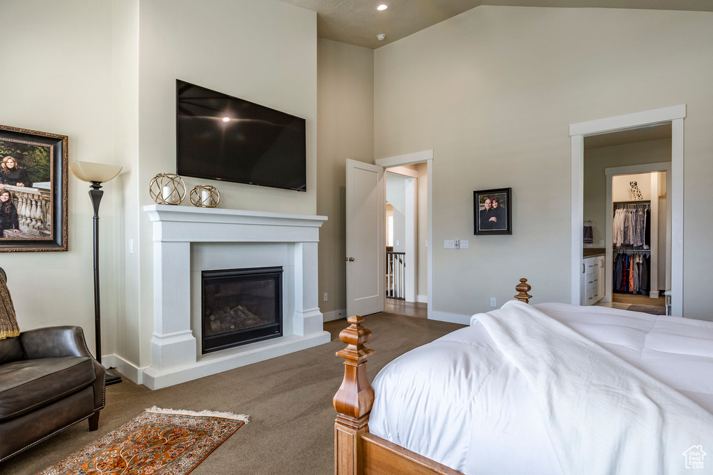 Bedroom with high vaulted ceiling, connected bathroom, and dark colored carpet