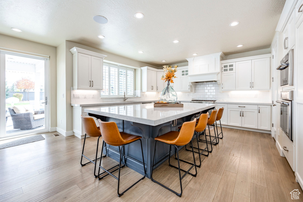 Kitchen with a kitchen island, decorative backsplash, a breakfast bar area, white cabinetry, and light hardwood / wood-style floors