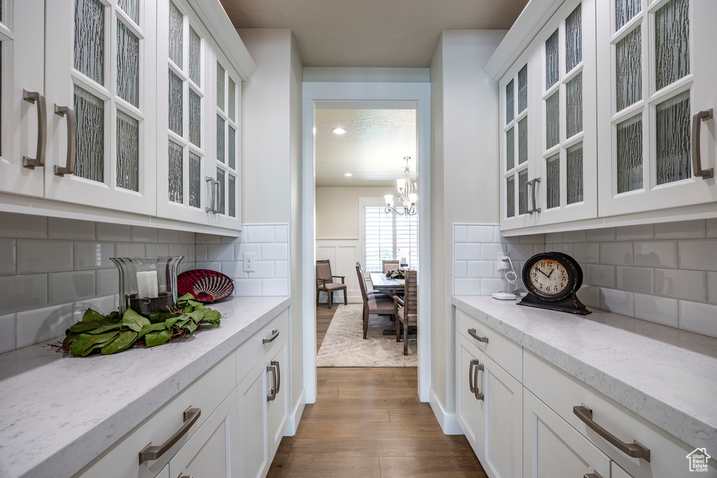 Bar with light stone countertops, white cabinets, hardwood / wood-style flooring, decorative backsplash, and an inviting chandelier