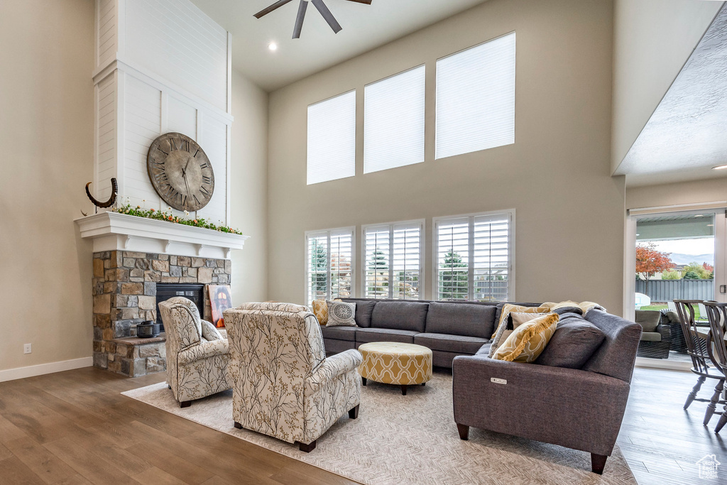 Living room with a towering ceiling, a stone fireplace, light hardwood / wood-style floors, and ceiling fan