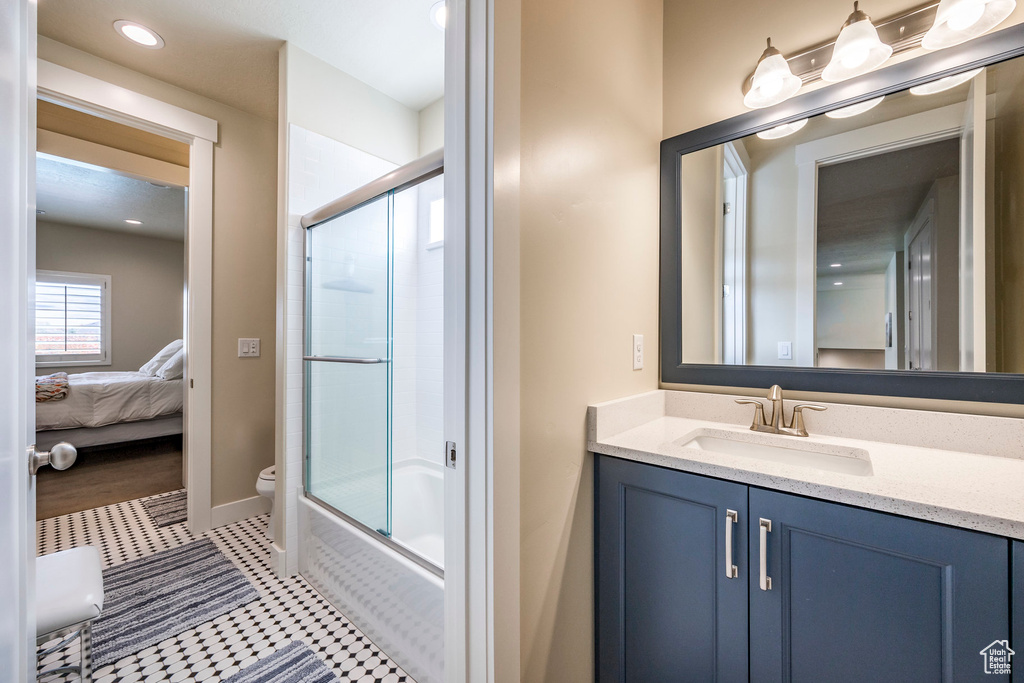 Full bathroom with vanity, bath / shower combo with glass door, and toilet