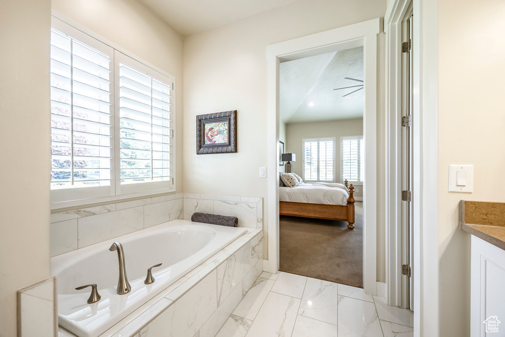 Bathroom featuring a wealth of natural light, vanity, and a relaxing tiled tub