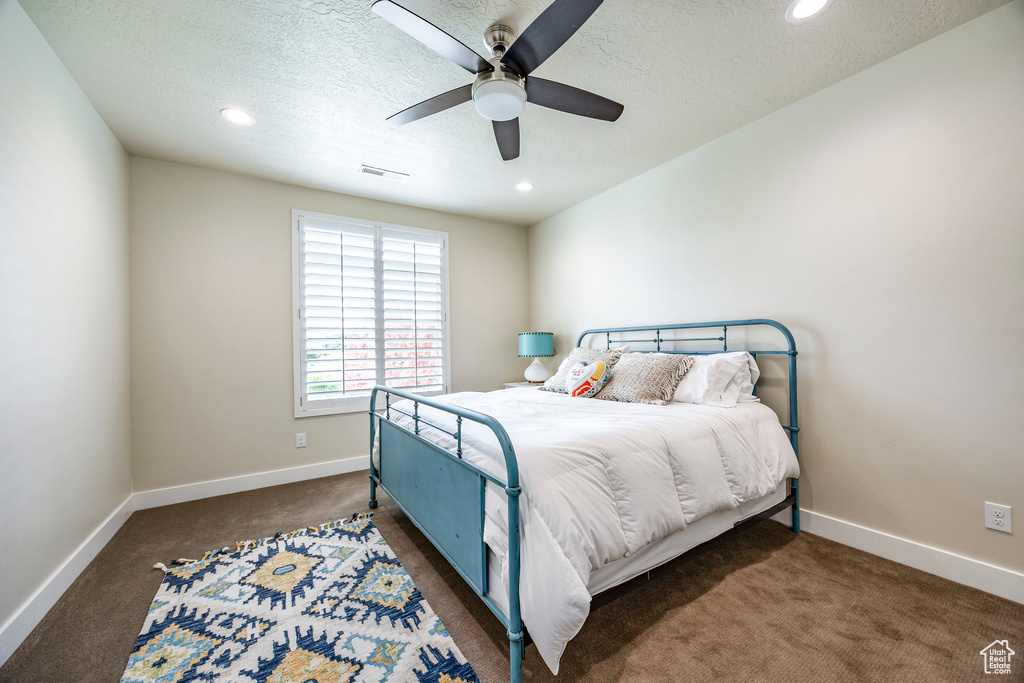 Bedroom featuring ceiling fan, a textured ceiling, and dark carpet