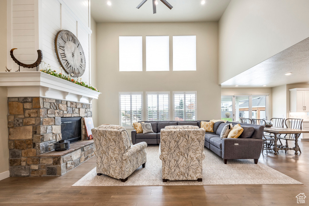 Living room featuring light hardwood / wood-style floors, a towering ceiling, a fireplace, and ceiling fan