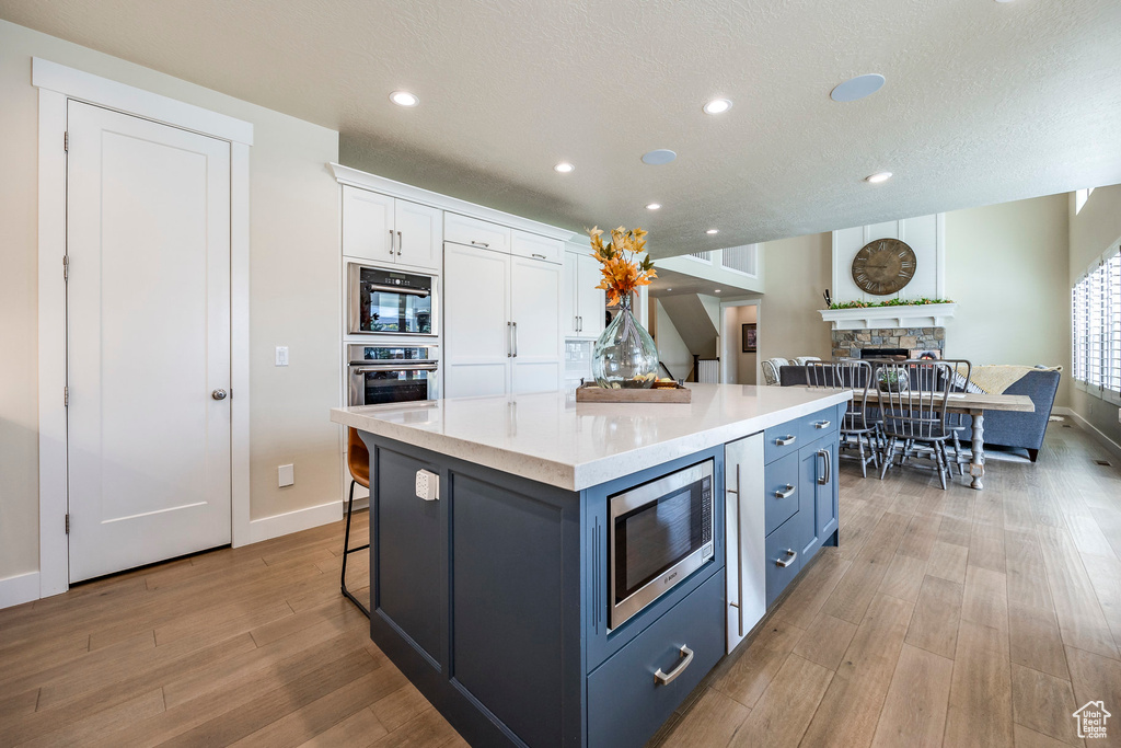 Kitchen with appliances with stainless steel finishes, a fireplace, a center island, white cabinetry, and light hardwood / wood-style flooring