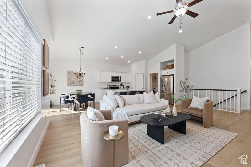 Living room with ceiling fan with notable chandelier, light wood-type flooring, and high vaulted ceiling