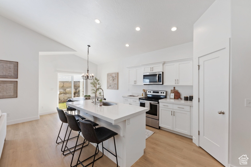 Kitchen featuring lofted ceiling, a center island with sink, white cabinets, and appliances with stainless steel finishes