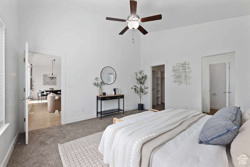 Bedroom featuring ceiling fan with notable chandelier, carpet flooring, a spacious closet, and a high ceiling