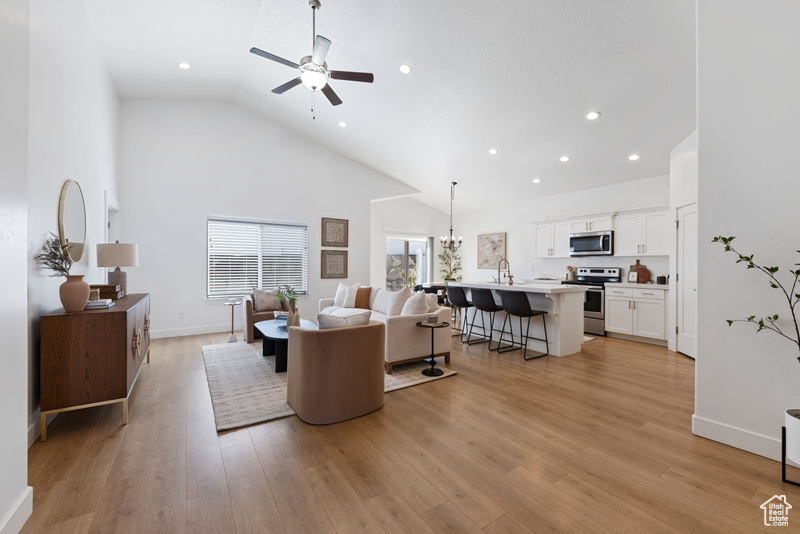 Living room with ceiling fan, light hardwood / wood-style flooring, sink, and high vaulted ceiling