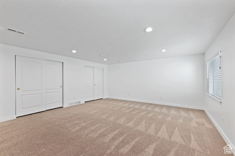 Unfurnished bedroom with multiple closets, a textured ceiling, and light carpet