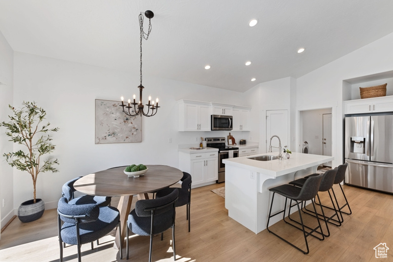 Kitchen featuring a center island with sink, sink, stainless steel appliances, hanging light fixtures, and white cabinets