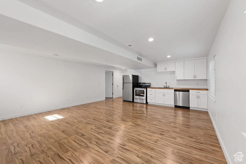 Kitchen featuring white cabinets, sink, wooden counters, light hardwood / wood-style flooring, and stainless steel appliances