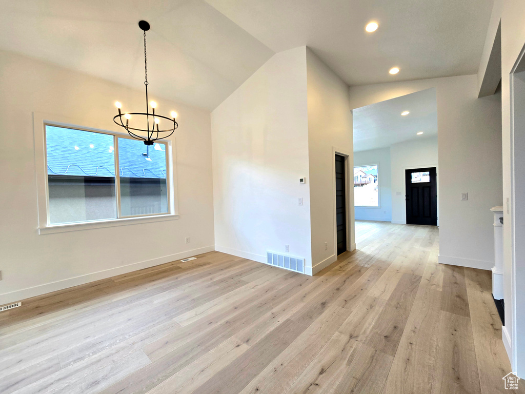 Unfurnished dining area with light hardwood / wood-style flooring, lofted ceiling, and a notable chandelier