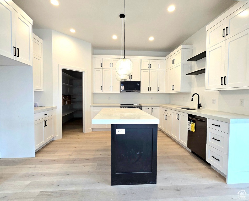 Kitchen featuring a kitchen island, black dishwasher, sink, decorative light fixtures, and white cabinets