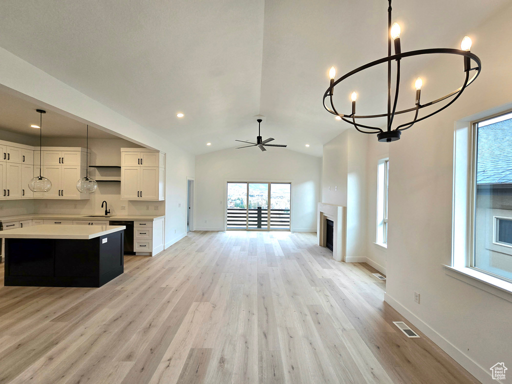 Kitchen with pendant lighting, lofted ceiling, white cabinets, sink, and light hardwood / wood-style flooring