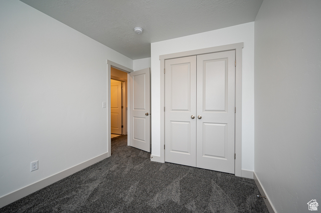 Unfurnished bedroom with a closet, a textured ceiling, and dark colored carpet