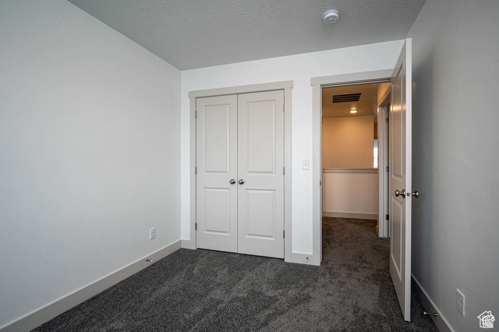 Unfurnished bedroom featuring a closet, a textured ceiling, and dark carpet