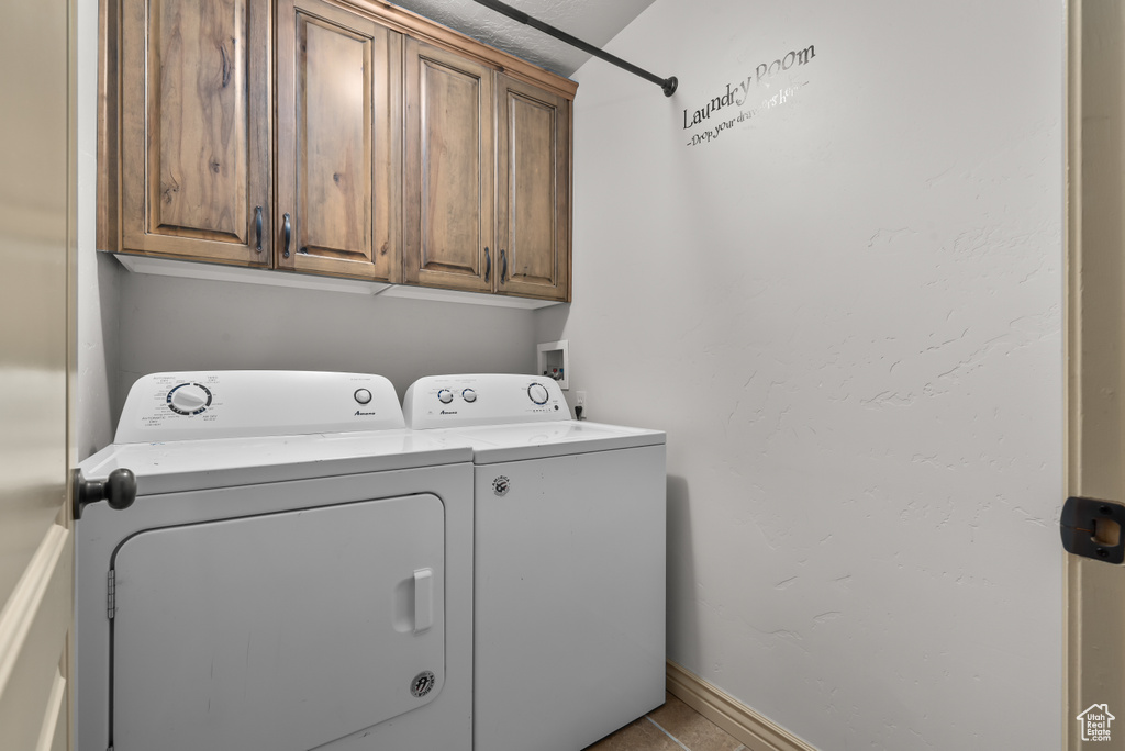 Clothes washing area featuring light tile patterned flooring, cabinets, and washing machine and clothes dryer