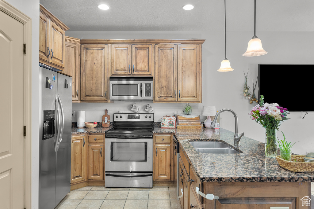 Kitchen featuring sink, stainless steel appliances, decorative light fixtures, dark stone countertops, and light tile patterned floors