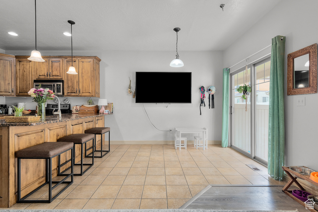 Kitchen with a breakfast bar area, hanging light fixtures, stainless steel appliances, dark stone counters, and light tile patterned floors