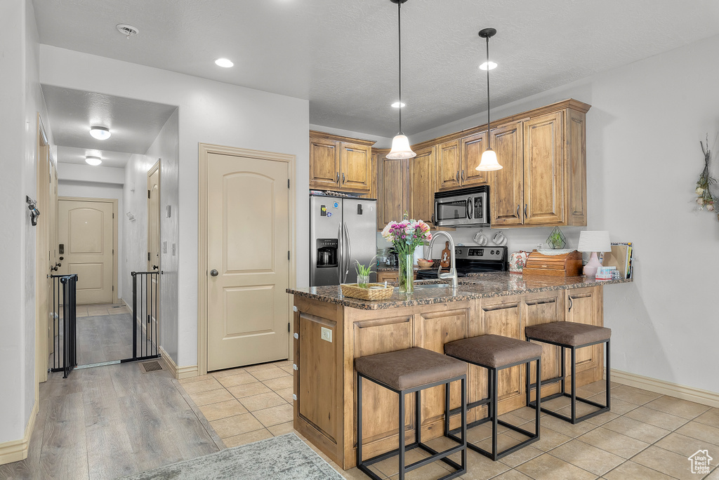 Kitchen featuring kitchen peninsula, appliances with stainless steel finishes, a breakfast bar, dark stone counters, and light wood-type flooring