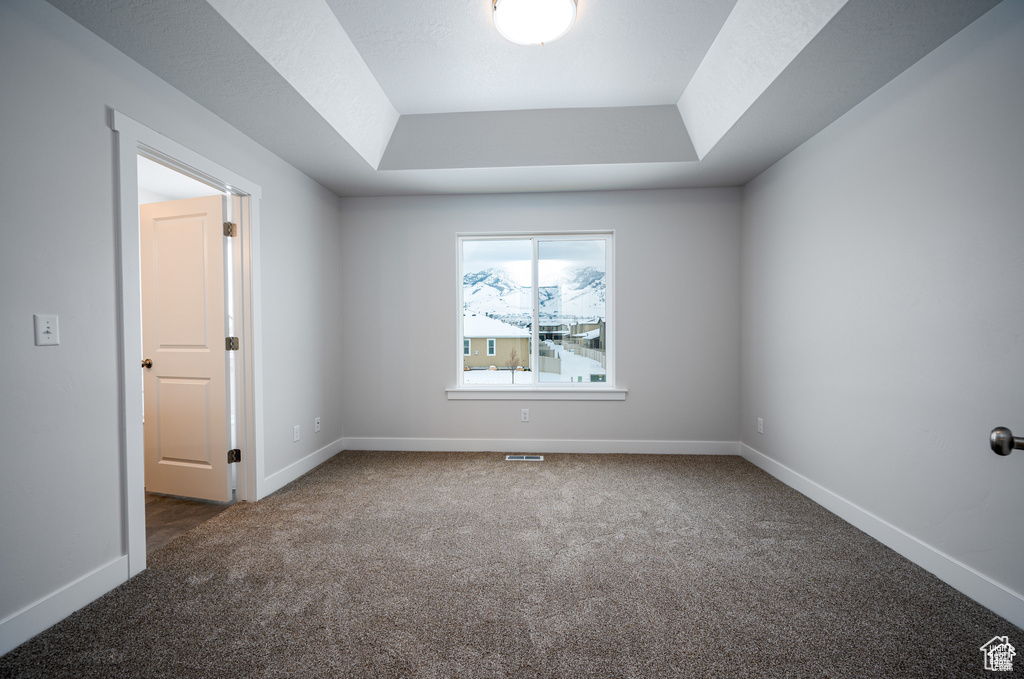 Empty room with a raised ceiling and dark colored carpet