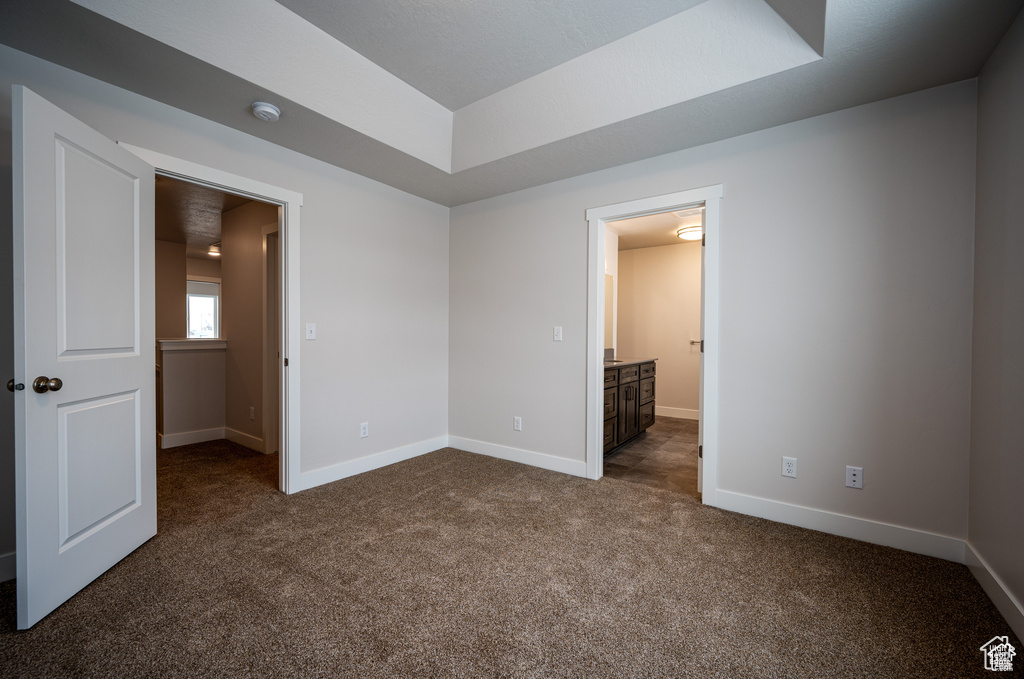 Unfurnished bedroom featuring ensuite bathroom and dark colored carpet