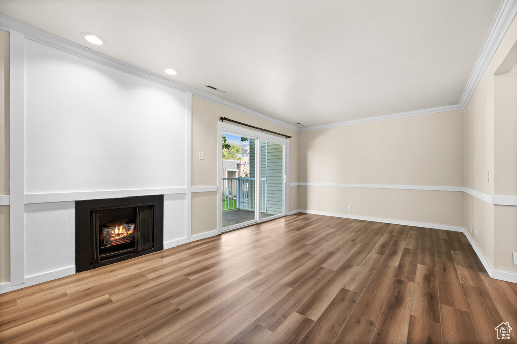 Unfurnished living room featuring ornamental molding and wood-type flooring