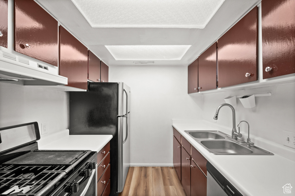 Kitchen with sink, appliances with stainless steel finishes, exhaust hood, and light hardwood / wood-style floors