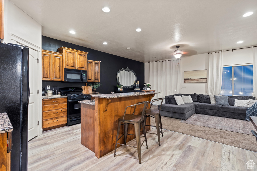 Kitchen featuring a kitchen breakfast bar, black appliances, light wood-type flooring, light stone counters, and ceiling fan