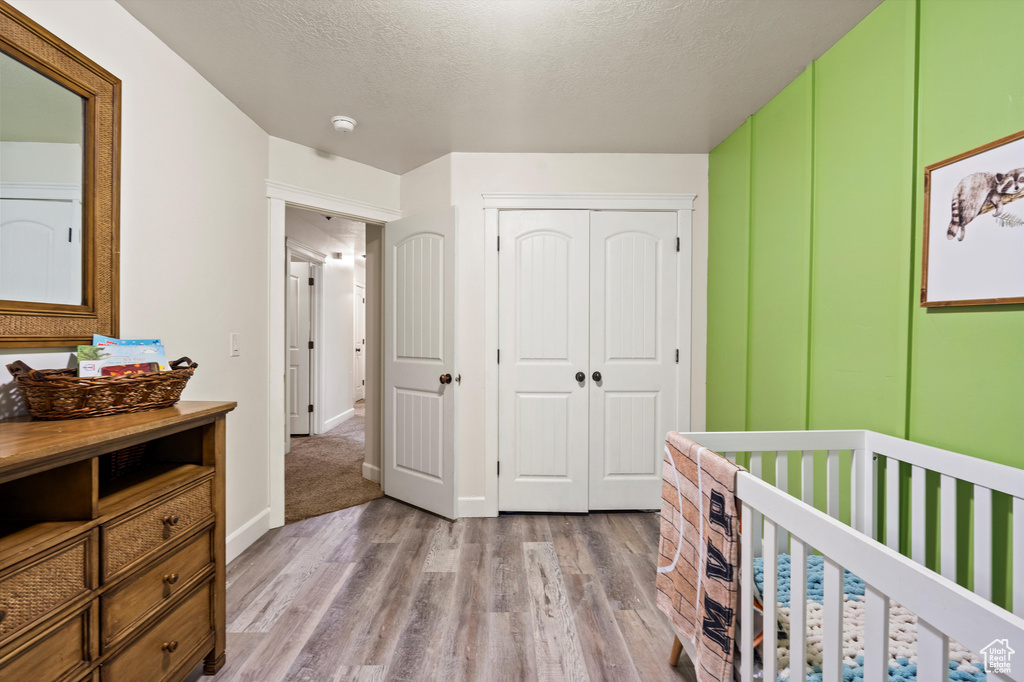 Bedroom featuring a closet, a textured ceiling, a crib, and light wood-type flooring