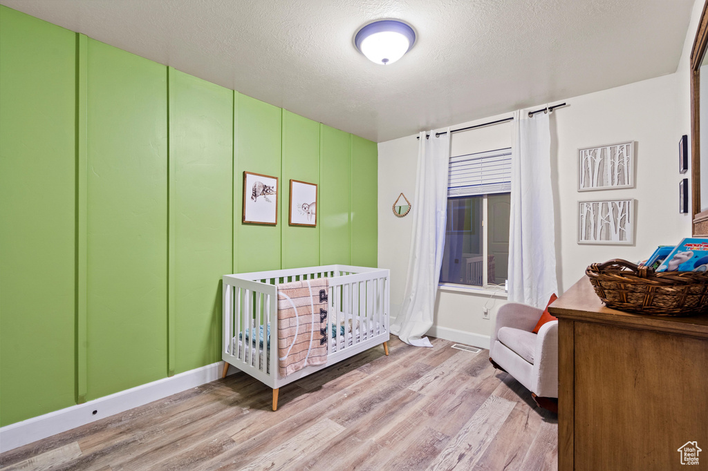 Bedroom with light hardwood / wood-style flooring, a textured ceiling, and a crib