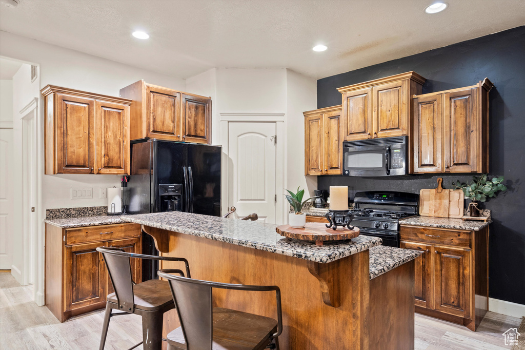 Kitchen featuring light stone counters, black appliances, a center island, and a kitchen bar