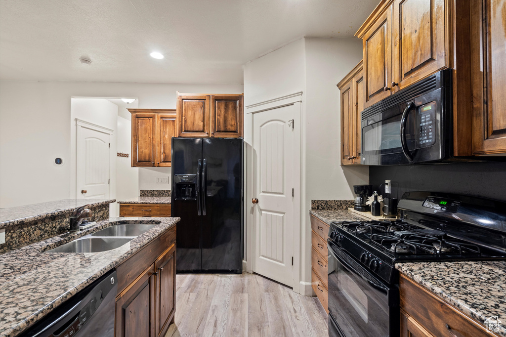 Kitchen featuring light hardwood / wood-style flooring, black appliances, sink, and dark stone counters