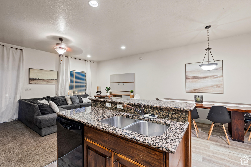 Kitchen featuring black dishwasher, hanging light fixtures, a center island with sink, sink, and light wood-type flooring