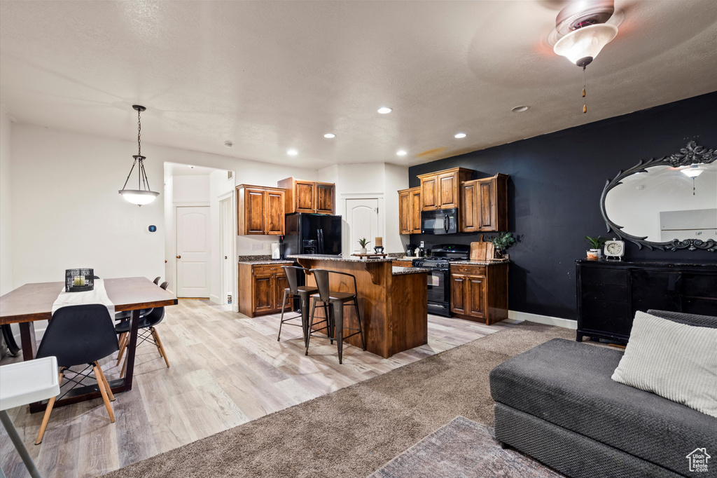 Kitchen featuring black appliances, light wood-type flooring, a kitchen breakfast bar, pendant lighting, and a center island with sink