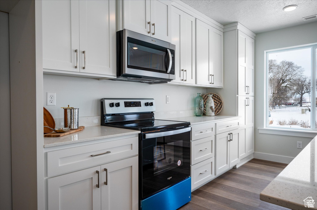 Kitchen with a textured ceiling, white cabinets, stainless steel appliances, and dark hardwood / wood-style floors